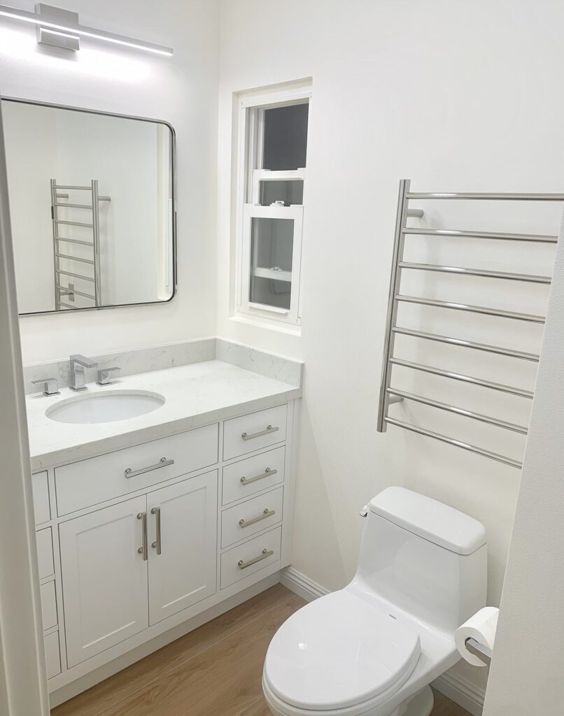 white finish bathroom, sink, mirror, metal drying rack and with cabinets